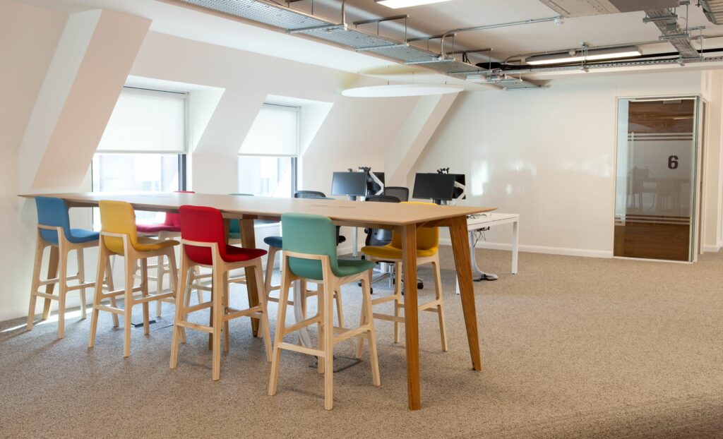 A light office space with a high table and a multi-coloured set of stools.