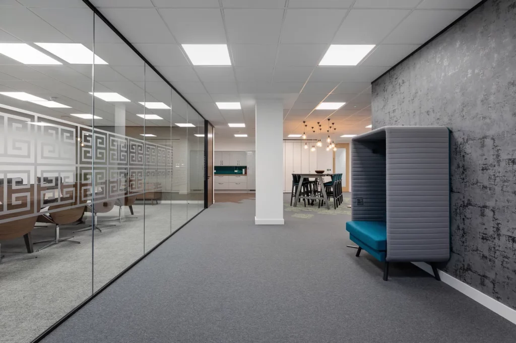 An office hallway with a glass wall and a boardroom behind it and a separate meeting pod.