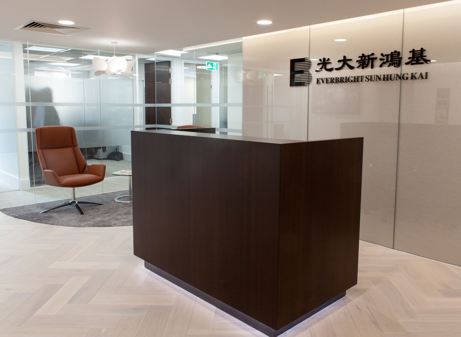 A modern reception area with a dark brown wooden reception desk that has custom floor lighting.