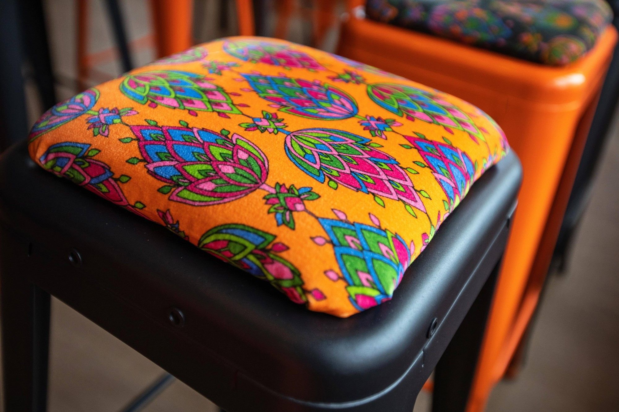 A black stool with an orange cushion with a colourful flower design.
