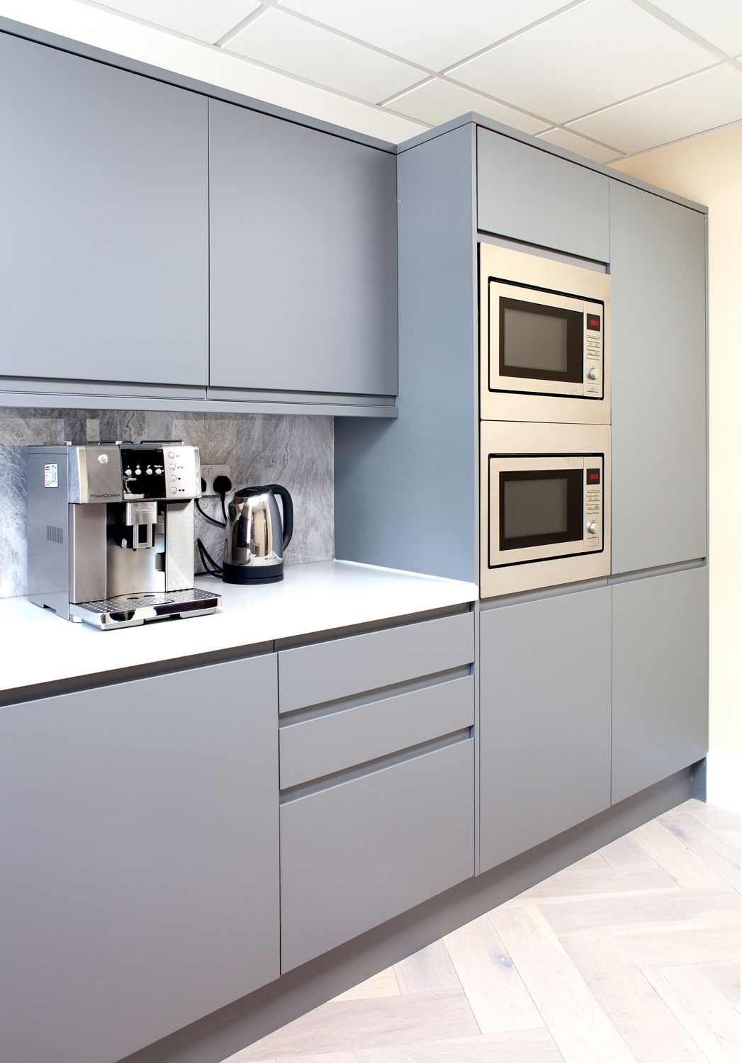 A kitchen space with grey cabinets, two microwaves and a coffee machine.