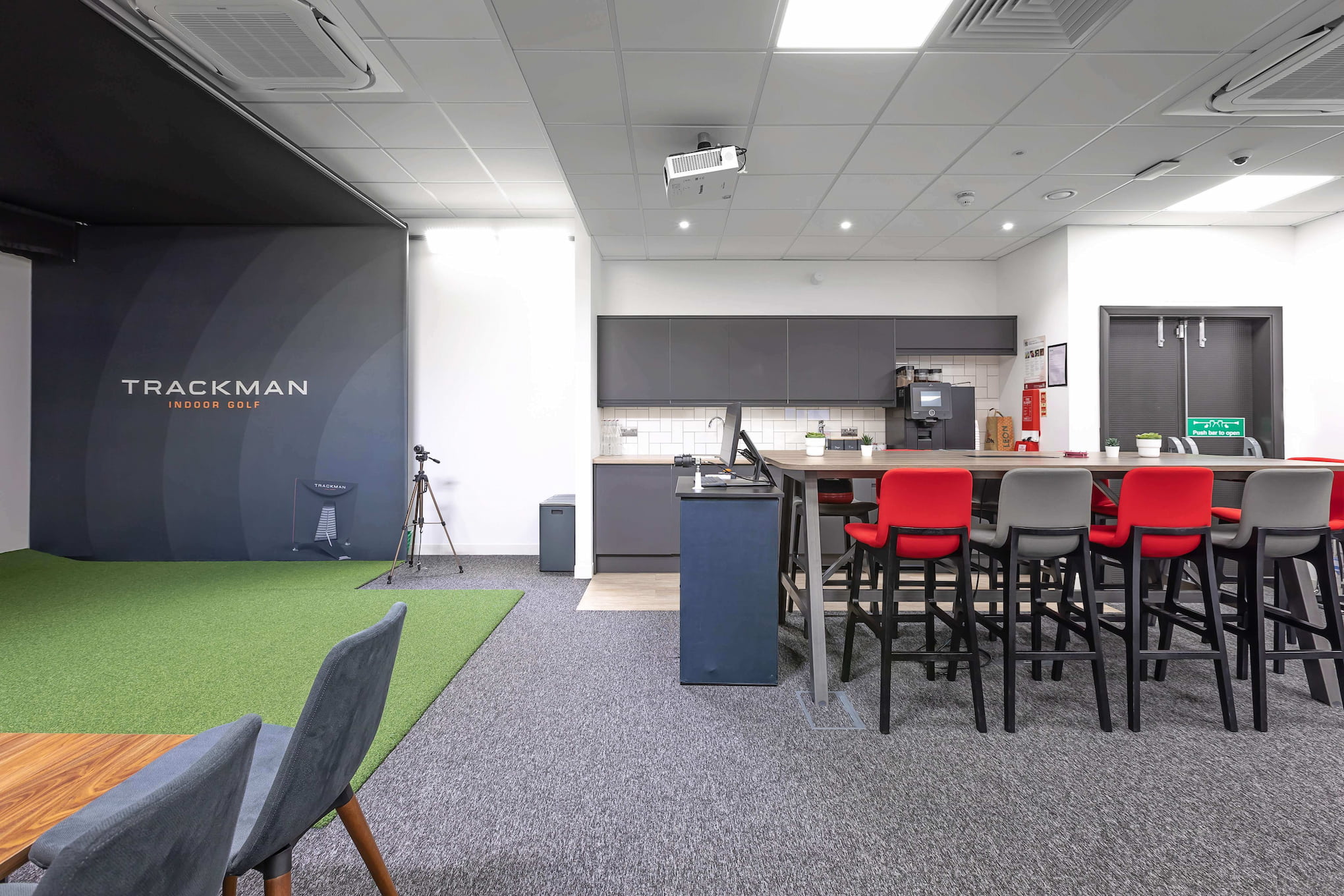 An office space with a kitchenette on the right and a golf simulator on the left.