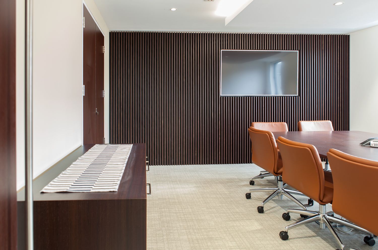 A meeting room with a sideboard, meeting table and a wall-mounted television.