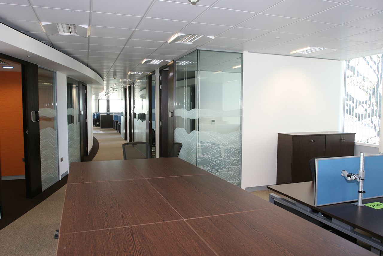 An office walk way with glass-partitioned meeting rooms either side.