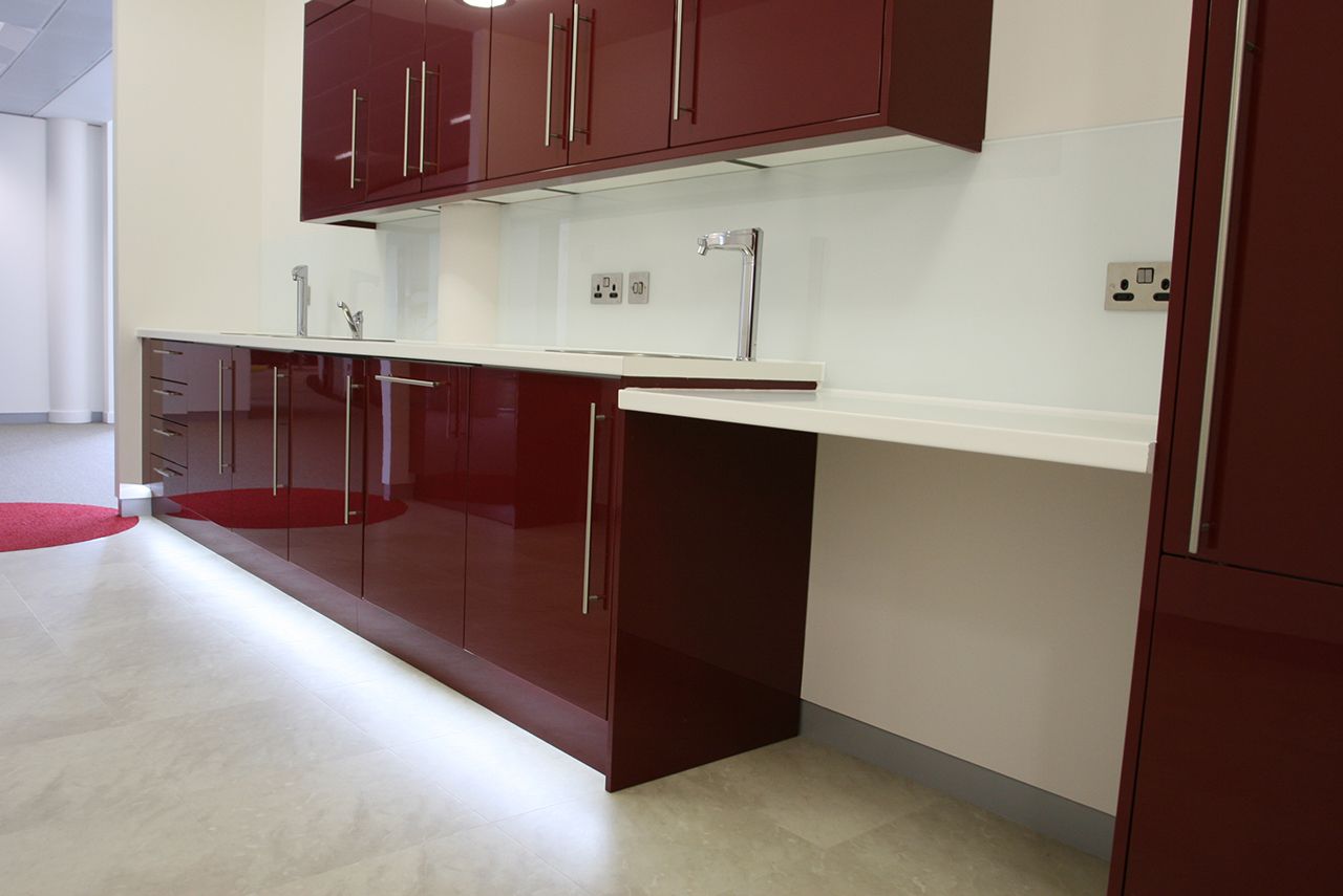 A kitchen with dark red cabinets with a gloss finish, built-in taps and wall plug sockets.