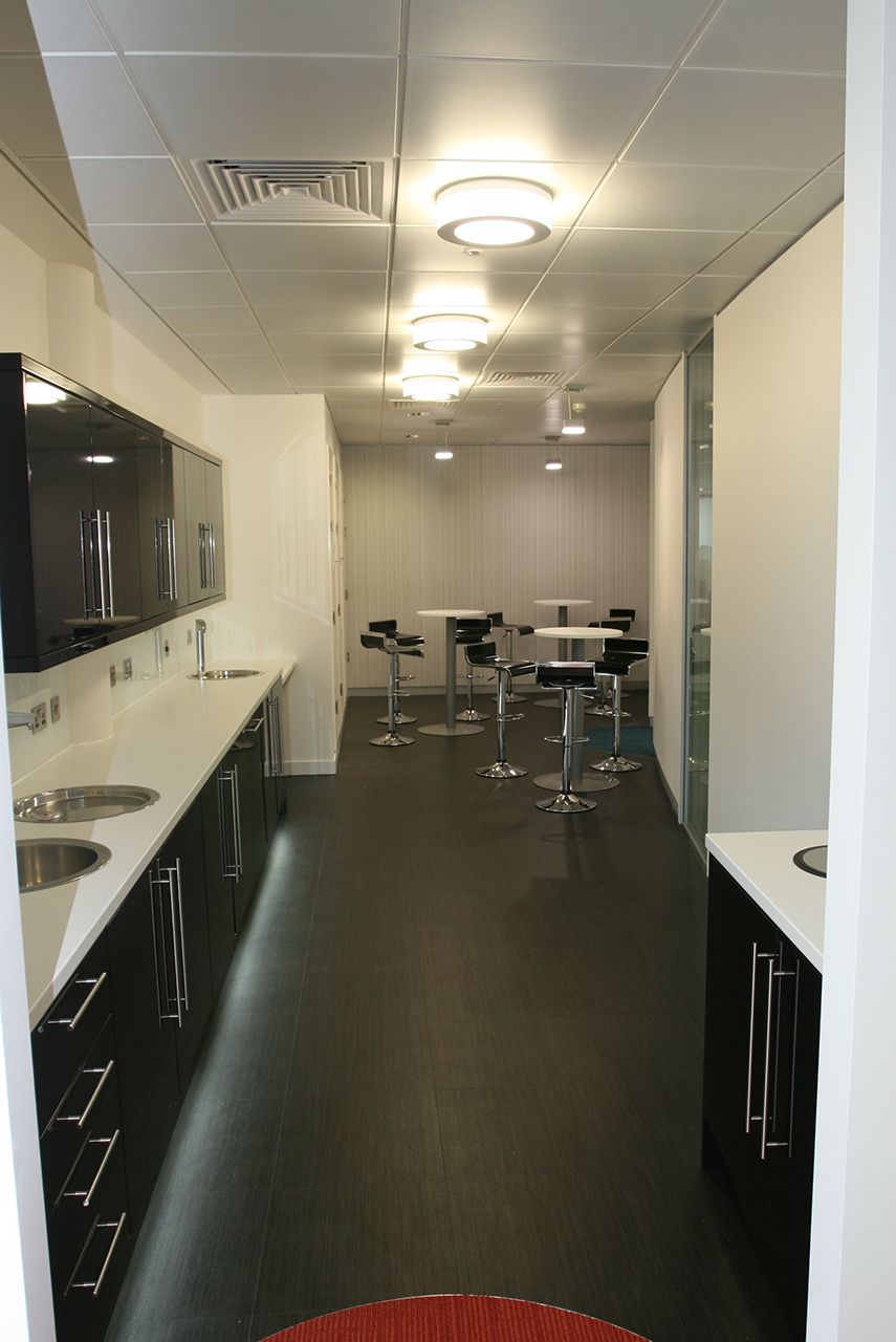 An office kitchen space with gloss black cabinets and high tables and stools.