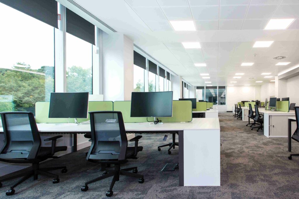 Office desks with screens, chairs and green space separators between them.