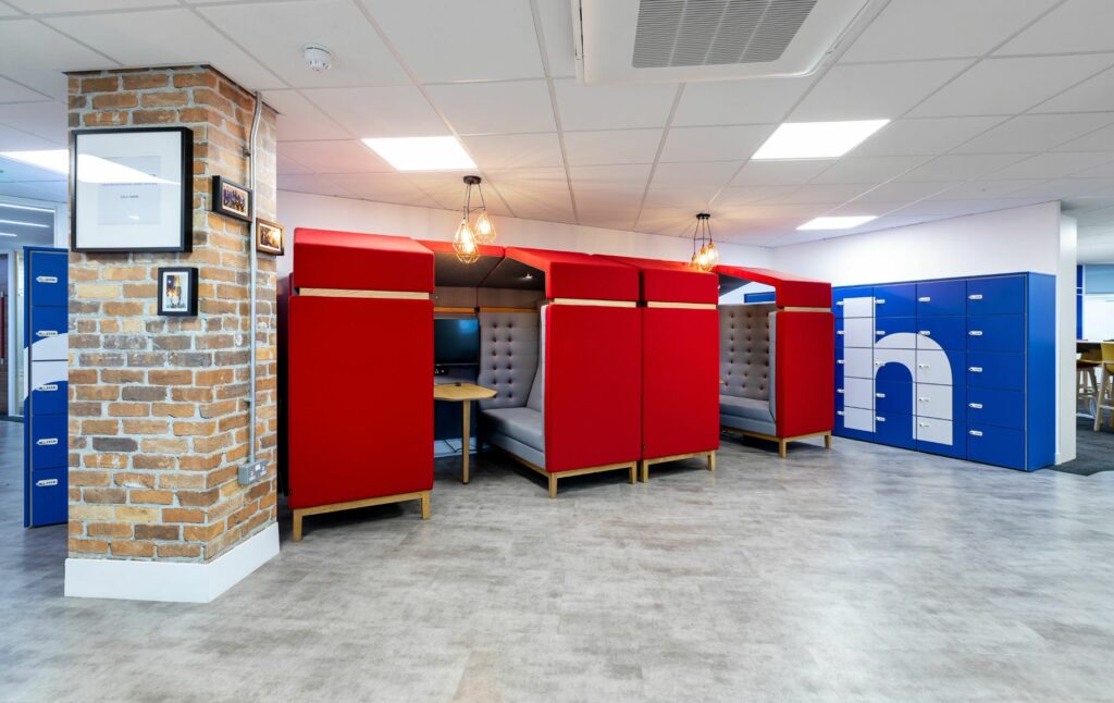 Private office working pods with grey sofas and televisions inside and blue lockers on the outside.